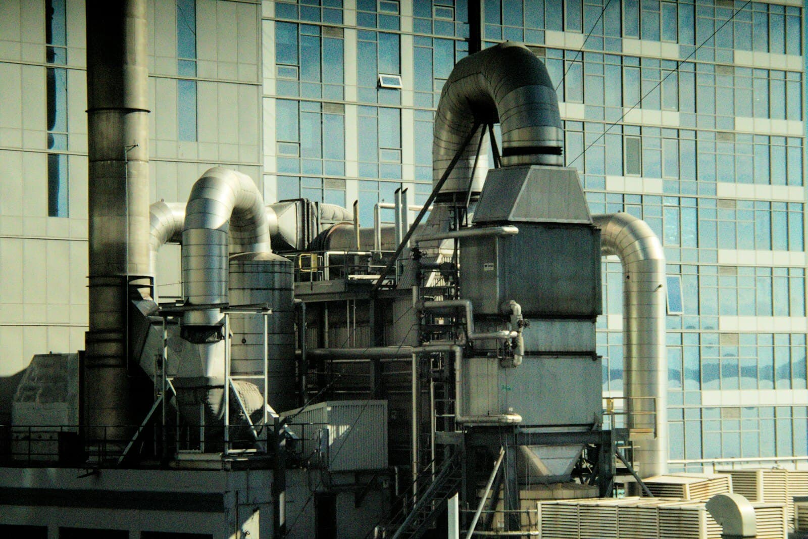 Building HVAC plant with air ducts and chilled-water pipework against an office tower
