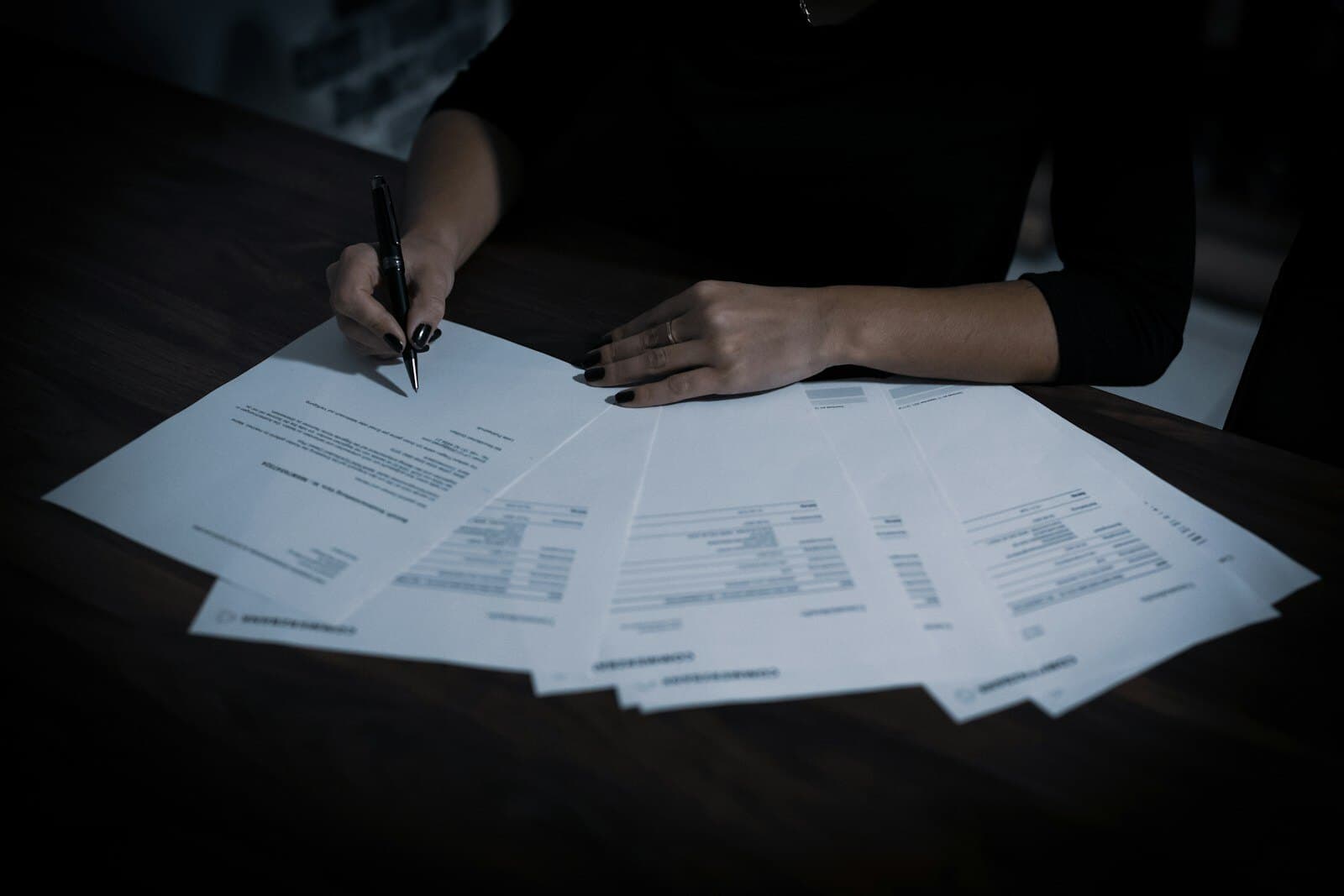 A person working through a fan of documents at a dark desk