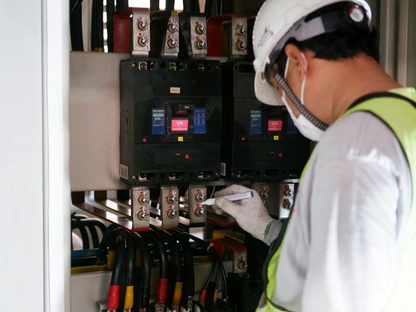 Technician inspecting a commercial electrical switchboard with moulded-case circuit breakers