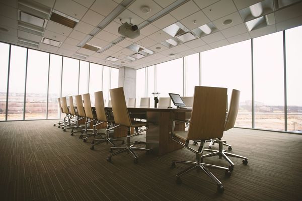 An empty boardroom with a long conference table and city-view windows