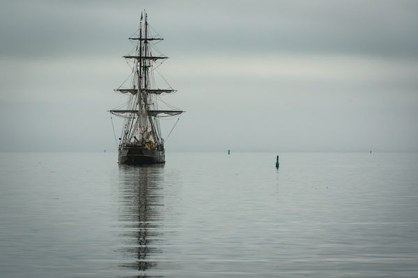 A lone wooden tall ship on calm grey water